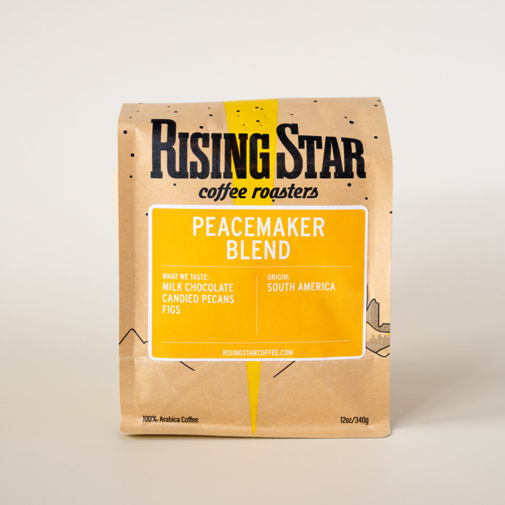 A Rising Star Coffee bag with a golden yellow label that reads "Peacemaker Blend". This South American coffee has notes of milk chocolate, candied pecans, and figs.
