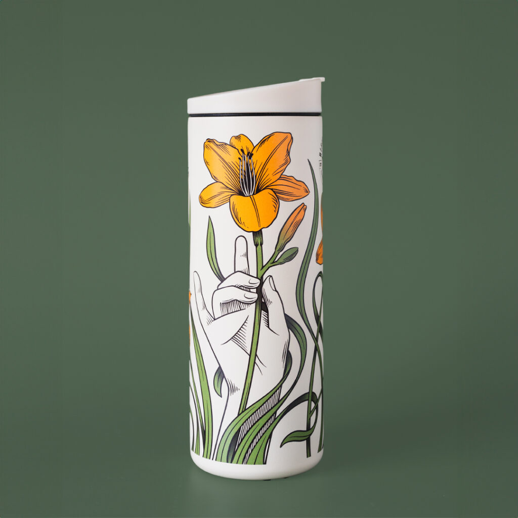 A white coffee travel tumbler with day lillies adorning the outside. It reads - 'one day at a time'