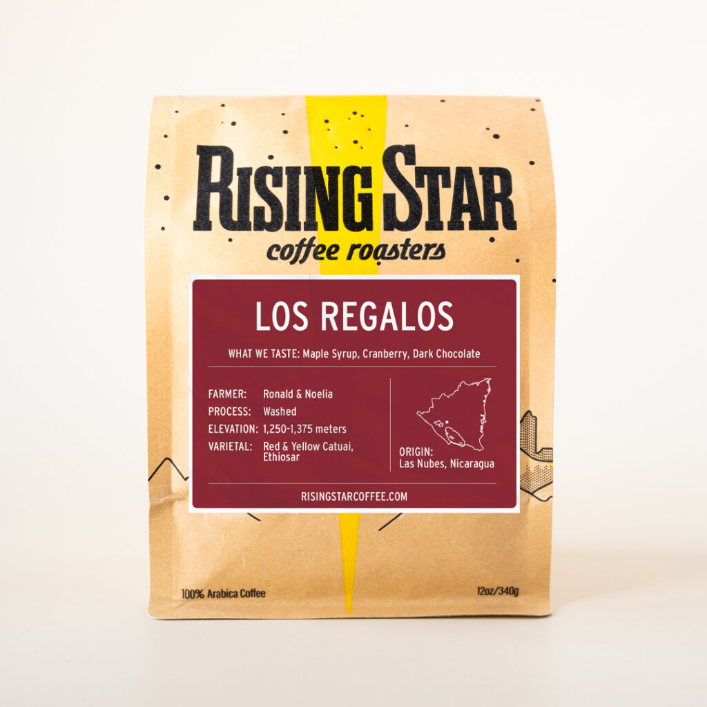 A tan bag of coffee from Rising Star Coffee Roasters with a deep cranberry red label that reads "Los Regalos".