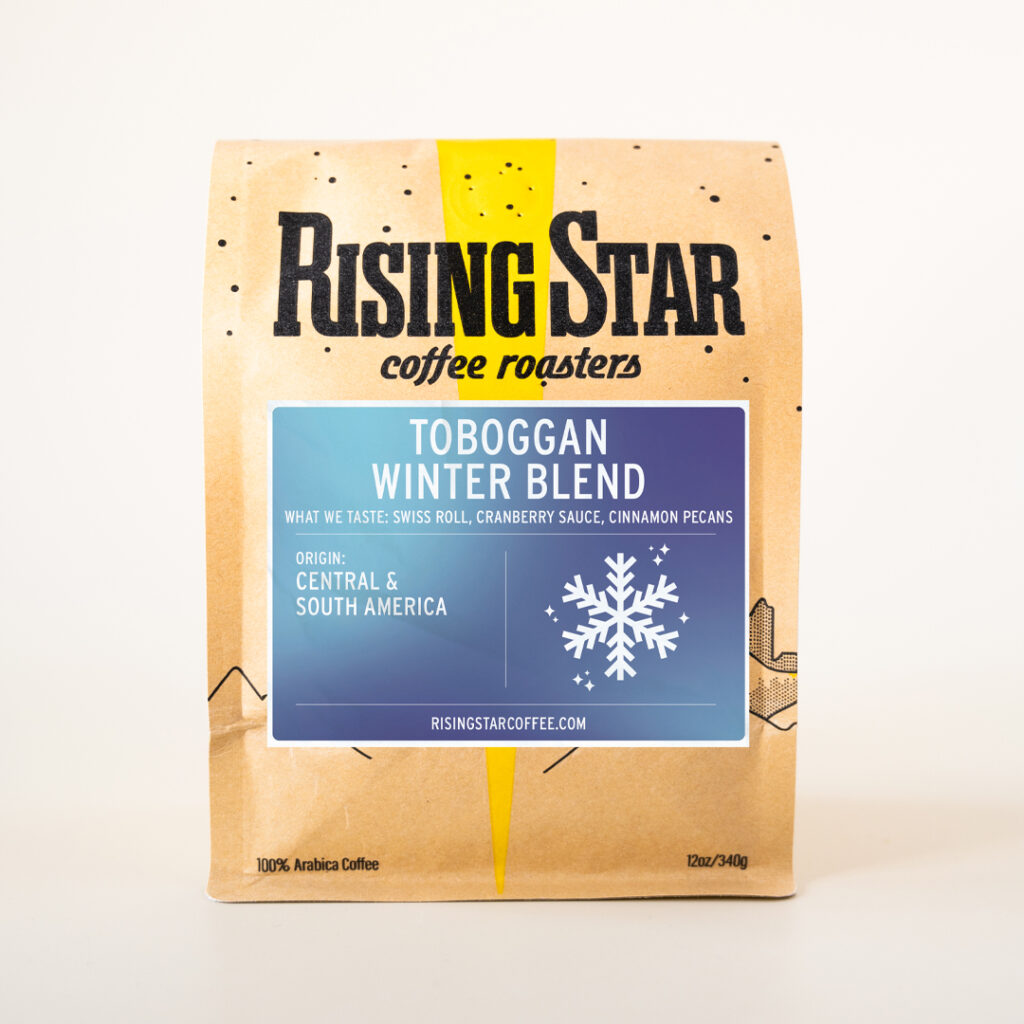 a bag of Rising Star Coffee's Toboggan Winter Blend. The blue gradient label has a snowflake graphic on it as well as the notes of Swiss Roll, Cranberry Sauce, and Cinnamon Pecans.