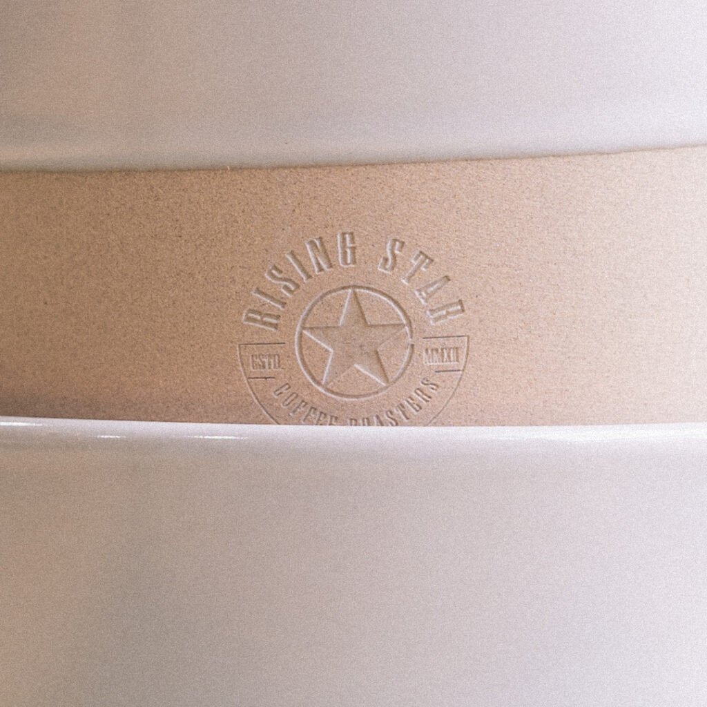 A close up of the stacked natural mugs - highlighting the etched Rising Star Coffee logo.