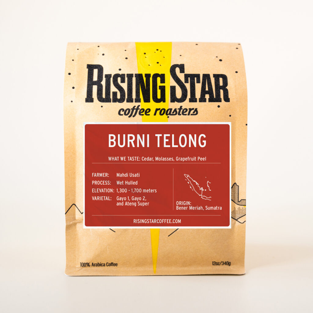 A brown bag of coffee from Rising Star Coffee Roasters with a red label reading “Burni Telong.” The label describes tasting notes of cedar, molasses, and grapefruit peel. It lists the farmer as Mahdi Usati, process as wet hulled, elevation 1,300–1,700 meters, and varietals Gayo 1, Gayo 2, and Ateng Super. The origin is Bener Meriah, Sumatra, with a small map outline of Sumatra. The bag is 12oz (340g) of 100% Arabica coffee.