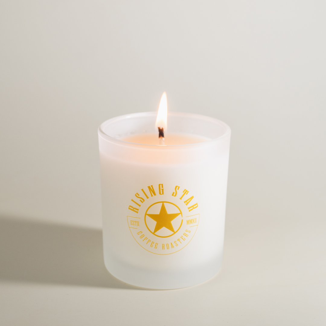 A white candle burning with a yellow Rising Star logo.