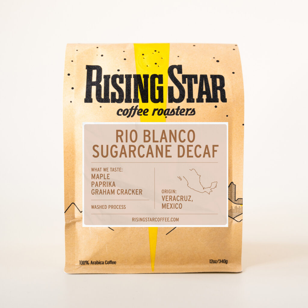 A tan bag of Rising Star Coffee with a cream colored label and contrasting brown text that reads: Rio Blanco Sugarcane Decaf. Veracruz, Mexico. 100% Arabica coffee. What we taste: Graham cracker, paprika, maple.